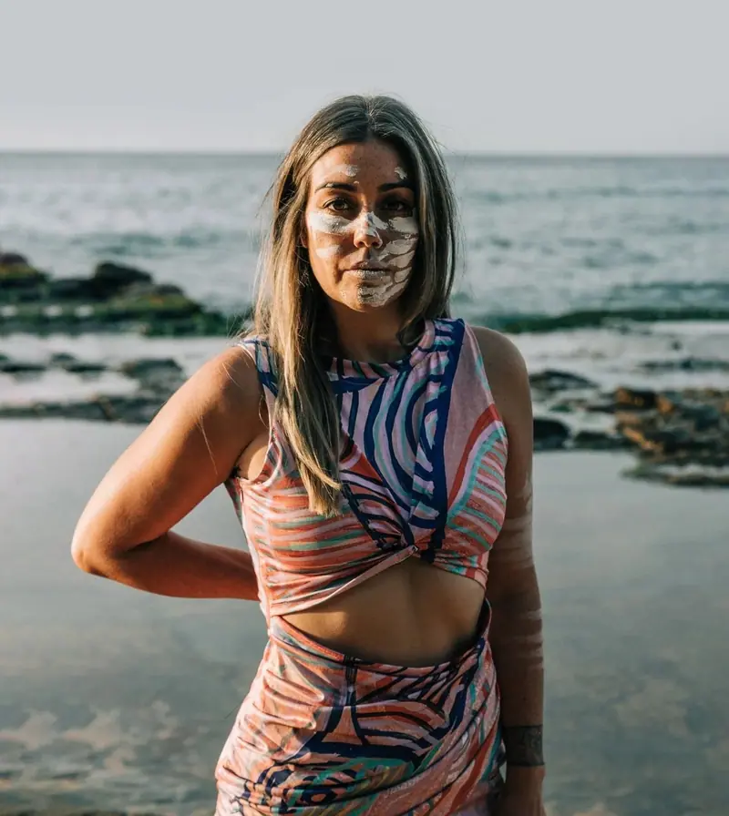 Renae Lamb in the ocean shallows on Worimi Country, ochre across her face, wearing her own design