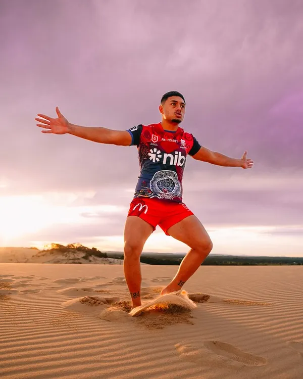 A player with arms wide on the dunes under a purple and pink sky