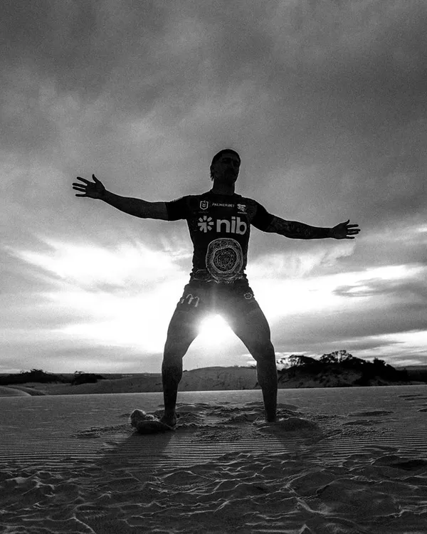 A player silhouetted with arms wide, the sun behind, in monochrome