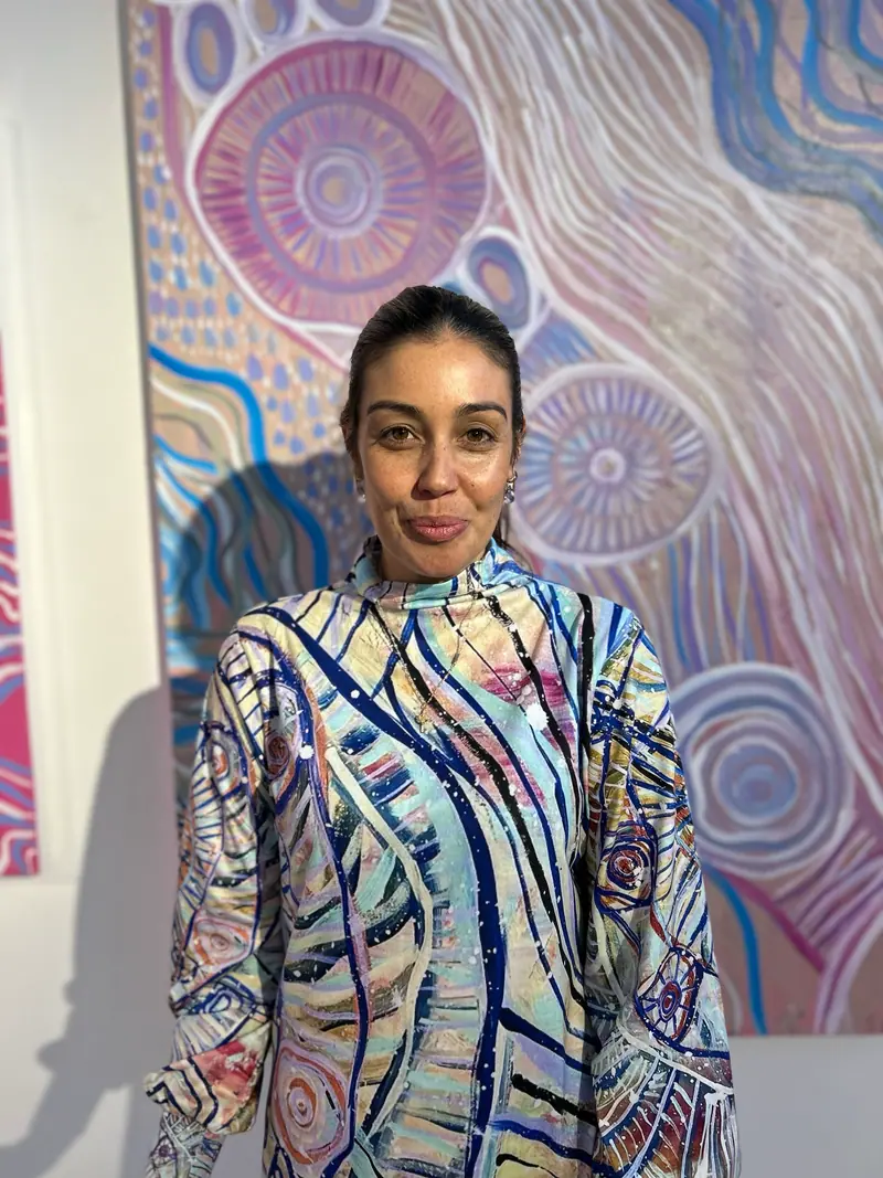 Renae Lamb in her own design, in front of her painting at an exhibition