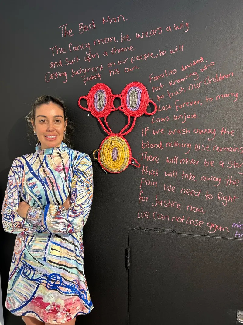 Renae Lamb in a printed dress beside her handwritten poem The Bad Man and her coral and yellow weavings