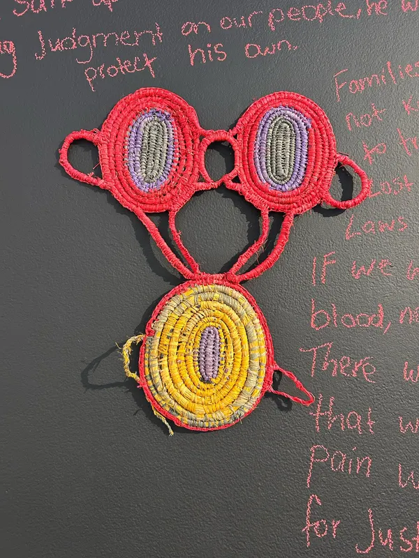 Coral and yellow woven forms by Renae Lamb on the wall carrying her poem The Bad Man